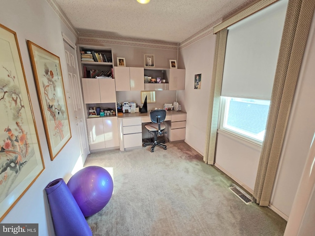 home office featuring ornamental molding, built in desk, light colored carpet, and a textured ceiling