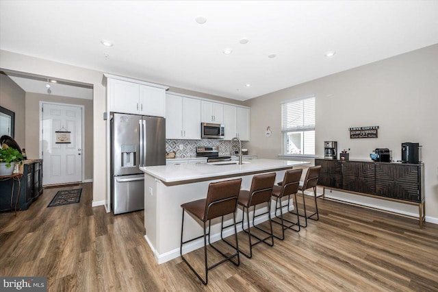 kitchen featuring a kitchen island with sink, backsplash, stainless steel appliances, white cabinets, and a kitchen bar