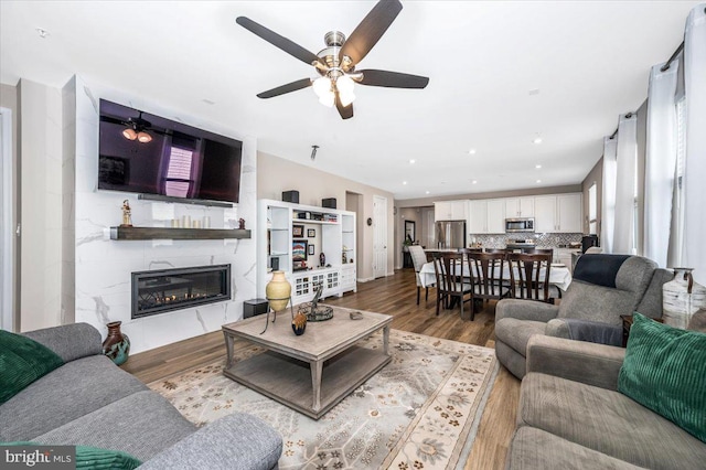 living room with wood-type flooring, ceiling fan, and a fireplace