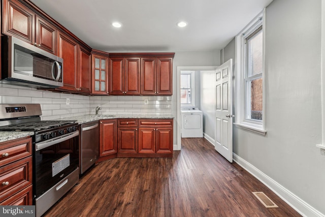 kitchen featuring stainless steel appliances, dark hardwood / wood-style floors, tasteful backsplash, light stone countertops, and washer / dryer