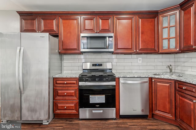 kitchen with sink, appliances with stainless steel finishes, backsplash, dark hardwood / wood-style floors, and light stone countertops