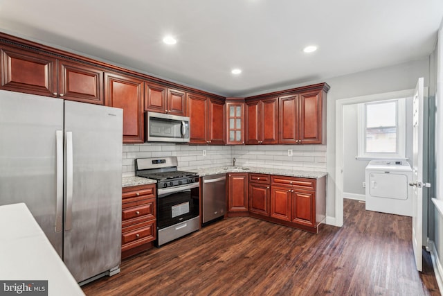 kitchen with stainless steel appliances, dark hardwood / wood-style floors, light stone countertops, decorative backsplash, and washer / dryer