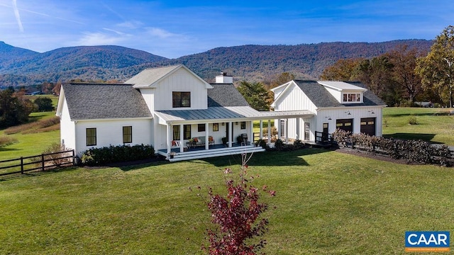 rear view of property featuring a garage, a mountain view, covered porch, and a lawn