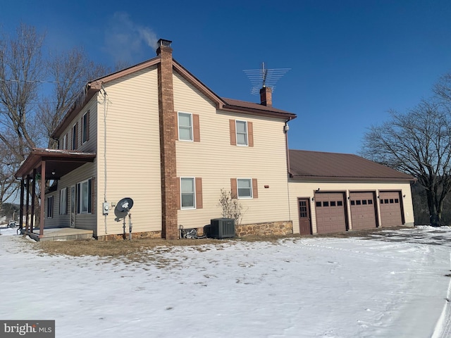 snow covered property featuring central AC unit and a garage