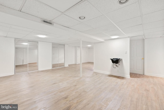 basement with a paneled ceiling and light wood-type flooring