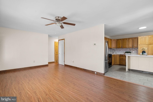 unfurnished living room with ceiling fan, sink, and light wood-type flooring