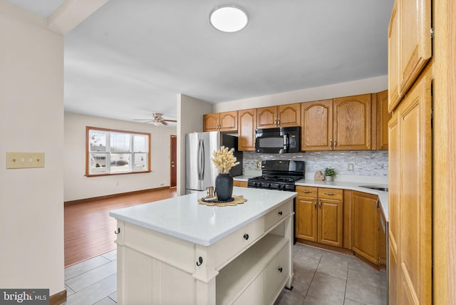 kitchen with light tile patterned floors, ceiling fan, black appliances, a kitchen island, and decorative backsplash