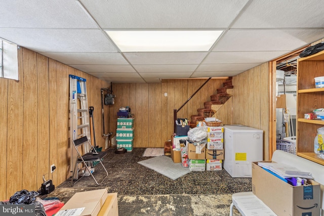 basement featuring a paneled ceiling, refrigerator, and wood walls