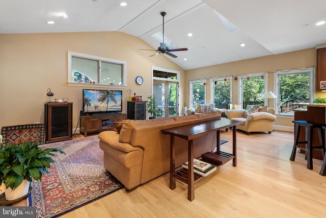 living room featuring ceiling fan, french doors, vaulted ceiling with skylight, and light wood-type flooring