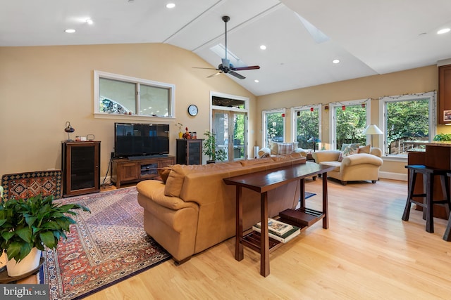 living room featuring lofted ceiling with skylight, ceiling fan, and light hardwood / wood-style flooring