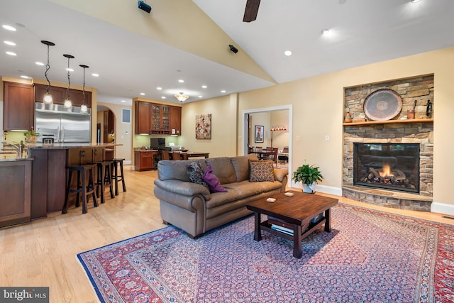 living room with high vaulted ceiling, a stone fireplace, light hardwood / wood-style floors, and ceiling fan