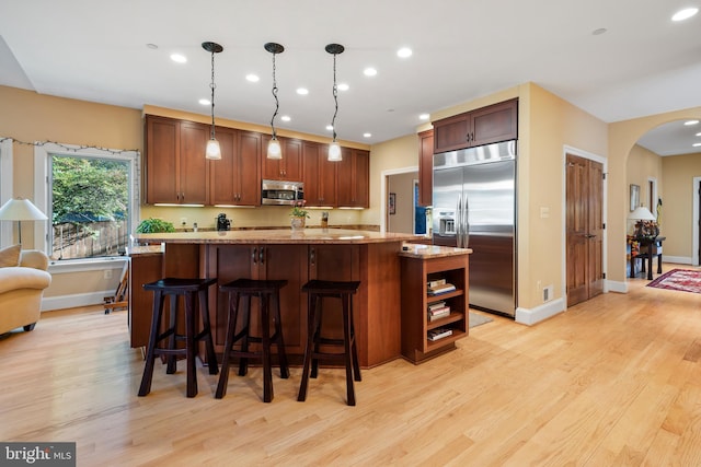 kitchen with stainless steel appliances, light hardwood / wood-style floors, hanging light fixtures, and a kitchen island