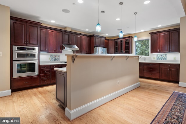 kitchen with a kitchen bar, decorative light fixtures, a center island, light wood-type flooring, and appliances with stainless steel finishes