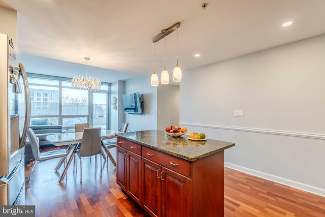 kitchen with dark stone countertops, hanging light fixtures, hardwood / wood-style flooring, a center island, and stainless steel refrigerator with ice dispenser