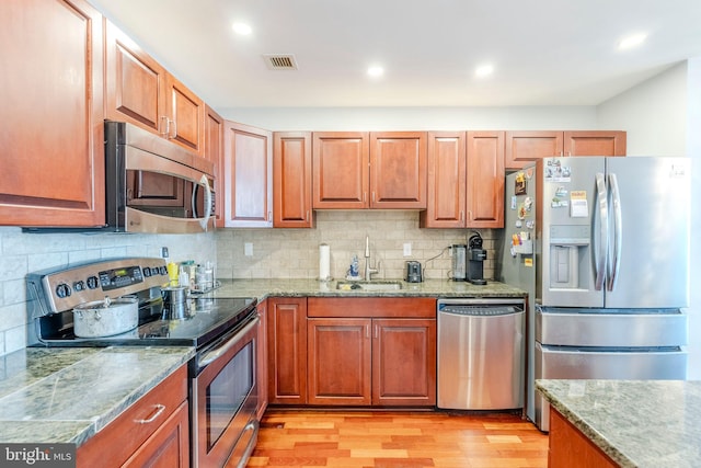 kitchen featuring appliances with stainless steel finishes, light hardwood / wood-style floors, sink, and backsplash