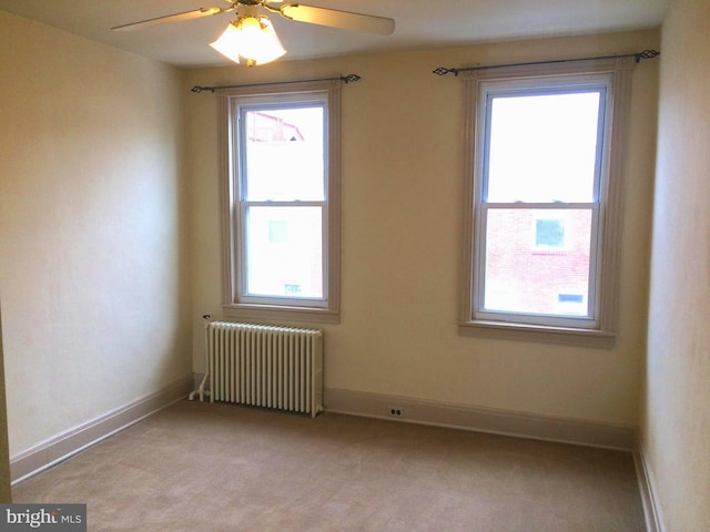 unfurnished room with ceiling fan, radiator, and light carpet