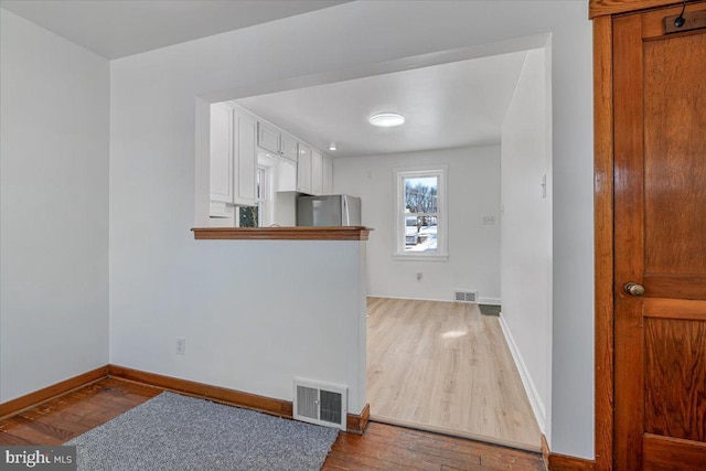 kitchen featuring hardwood / wood-style flooring, stainless steel fridge, and white cabinets