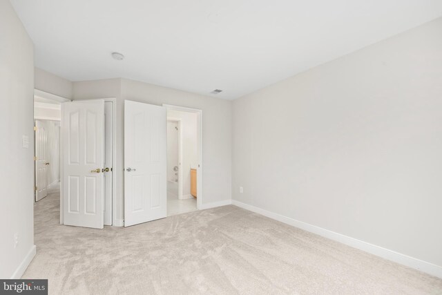 unfurnished bedroom featuring carpet floors, ensuite bath, visible vents, and baseboards