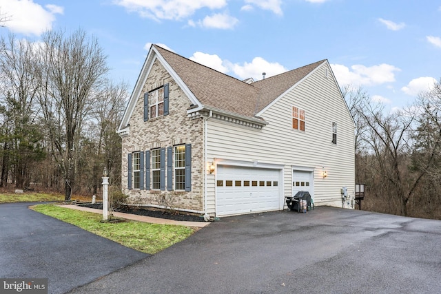 view of home's exterior featuring a garage, brick siding, roof with shingles, and aphalt driveway