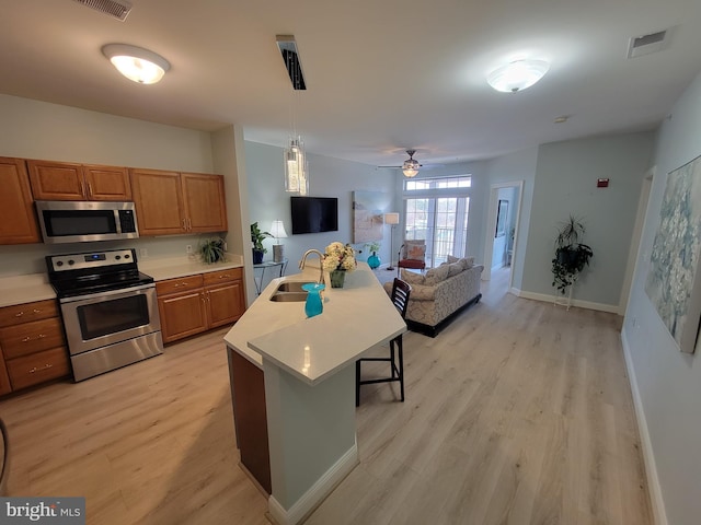 kitchen with a breakfast bar, sink, decorative light fixtures, appliances with stainless steel finishes, and a kitchen island with sink