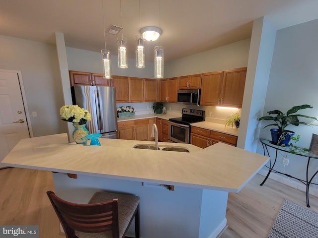 kitchen with appliances with stainless steel finishes, pendant lighting, sink, a breakfast bar area, and light wood-type flooring