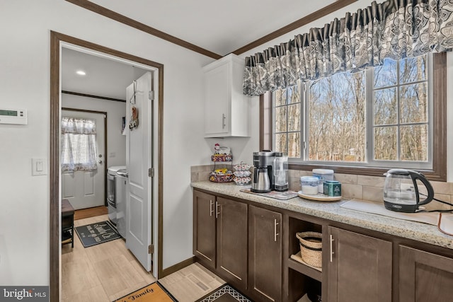 kitchen featuring white cabinetry, dark brown cabinetry, light stone countertops, ornamental molding, and washing machine and clothes dryer