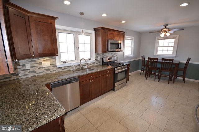 kitchen with pendant lighting, sink, stainless steel appliances, tasteful backsplash, and dark stone counters