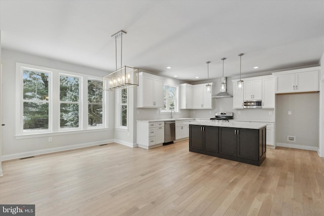 kitchen featuring pendant lighting, wall chimney range hood, a center island, and white cabinets