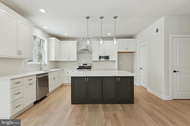 kitchen with white cabinetry, hanging light fixtures, a center island, stainless steel appliances, and wall chimney range hood