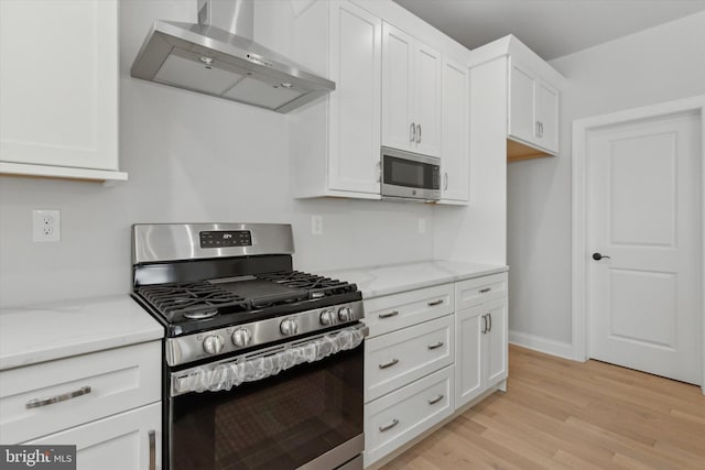 kitchen featuring white cabinets, light hardwood / wood-style floors, stainless steel appliances, light stone countertops, and wall chimney range hood