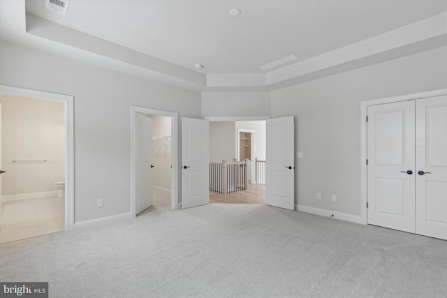 unfurnished bedroom featuring connected bathroom, light colored carpet, and a raised ceiling