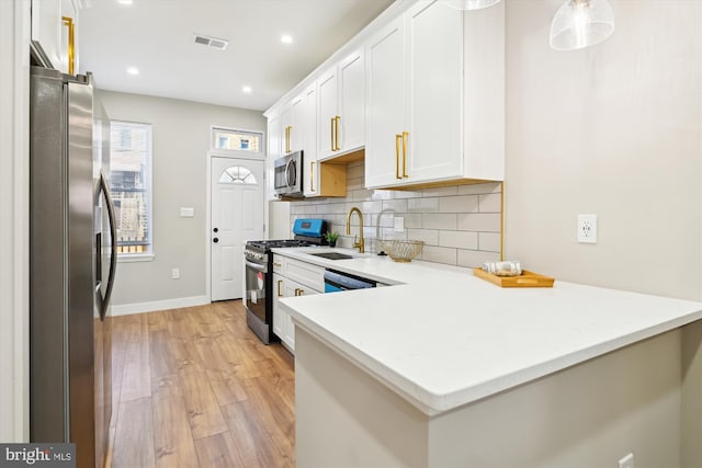 kitchen with appliances with stainless steel finishes, sink, white cabinets, decorative backsplash, and kitchen peninsula