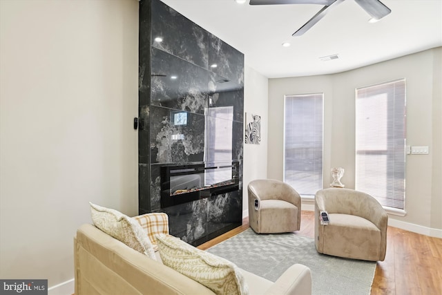 living room featuring wood-type flooring, plenty of natural light, a high end fireplace, and ceiling fan