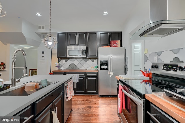 kitchen featuring sink, island range hood, appliances with stainless steel finishes, pendant lighting, and decorative backsplash