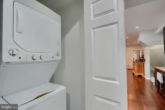 laundry room with dark hardwood / wood-style flooring and stacked washing maching and dryer