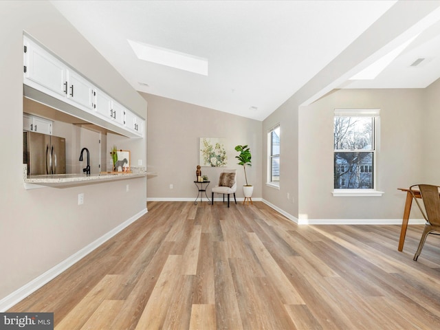 bar with stainless steel refrigerator, white cabinetry, vaulted ceiling with skylight, light stone counters, and light hardwood / wood-style floors