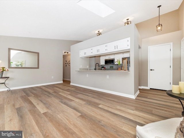 unfurnished living room with lofted ceiling with skylight, sink, and light hardwood / wood-style flooring