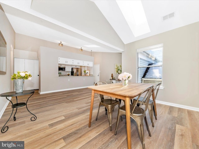 dining room with lofted ceiling with skylight and light hardwood / wood-style floors