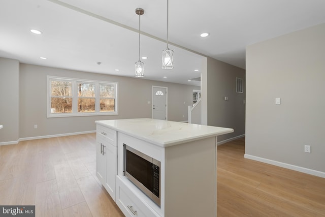 kitchen with white cabinetry, a center island, light wood-type flooring, pendant lighting, and light stone countertops