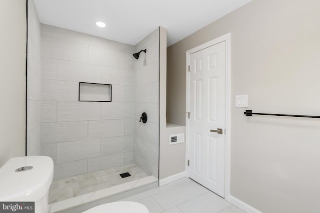 bathroom with tile patterned flooring, a tile shower, and toilet