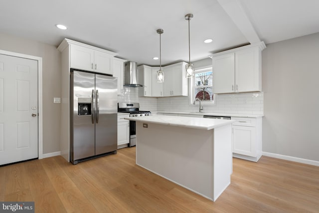 kitchen with white cabinetry, decorative light fixtures, appliances with stainless steel finishes, a kitchen island, and wall chimney range hood