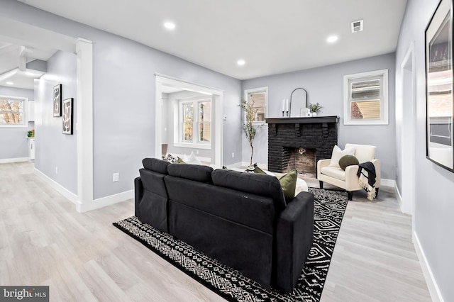 living room with a brick fireplace, a healthy amount of sunlight, and light hardwood / wood-style flooring