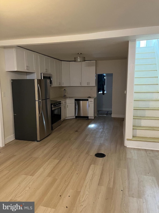 kitchen with white cabinetry, stainless steel appliances, sink, and light hardwood / wood-style floors