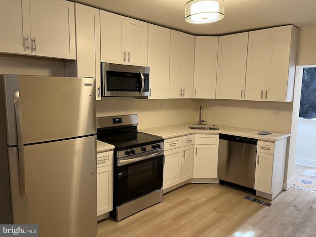 kitchen featuring appliances with stainless steel finishes, sink, white cabinets, and light hardwood / wood-style floors