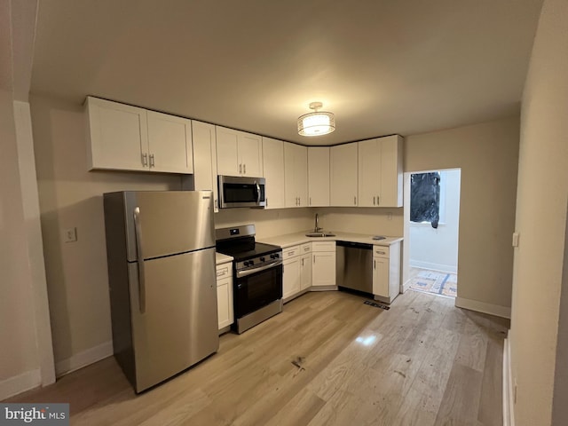 kitchen featuring stainless steel appliances, sink, white cabinets, and light wood-type flooring