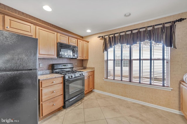 kitchen with light stone countertops, light tile patterned floors, black appliances, and light brown cabinets