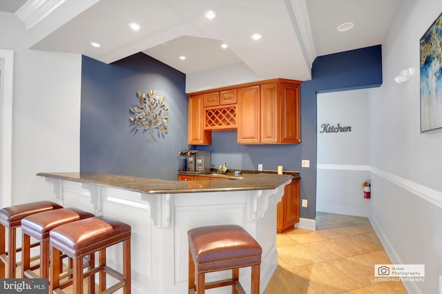 kitchen featuring crown molding, kitchen peninsula, a breakfast bar area, and light tile patterned floors