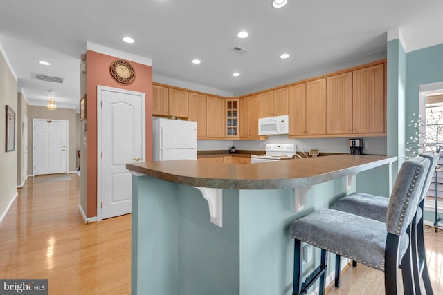 kitchen with a breakfast bar, kitchen peninsula, white appliances, and light hardwood / wood-style floors