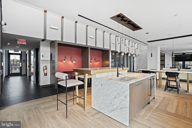 kitchen featuring a spacious island, sink, light stone counters, hanging light fixtures, and light parquet floors