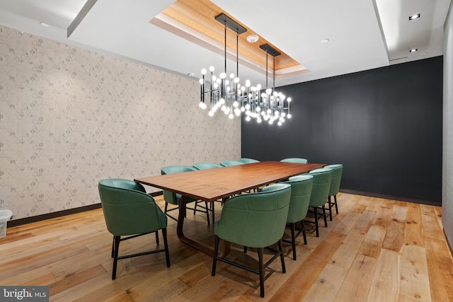 dining room with an inviting chandelier, a tray ceiling, and light wood-type flooring